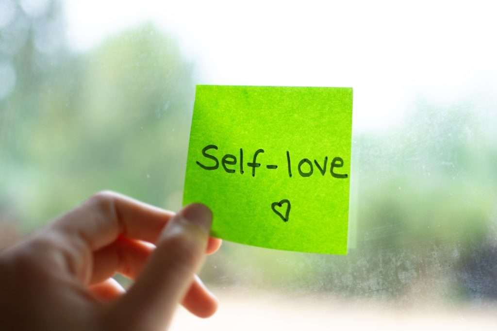 Hand holding green sticky note with self-love message promoting mental health awareness