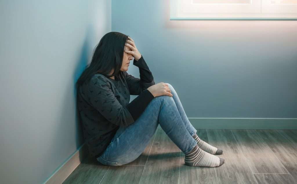 Woman with depression with hand on face sitting on the floor